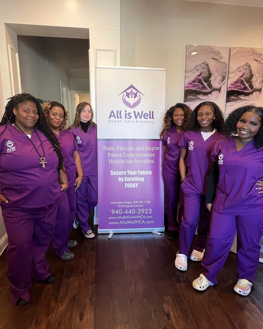 Cohort in purple scrubs beside the All is Well banner